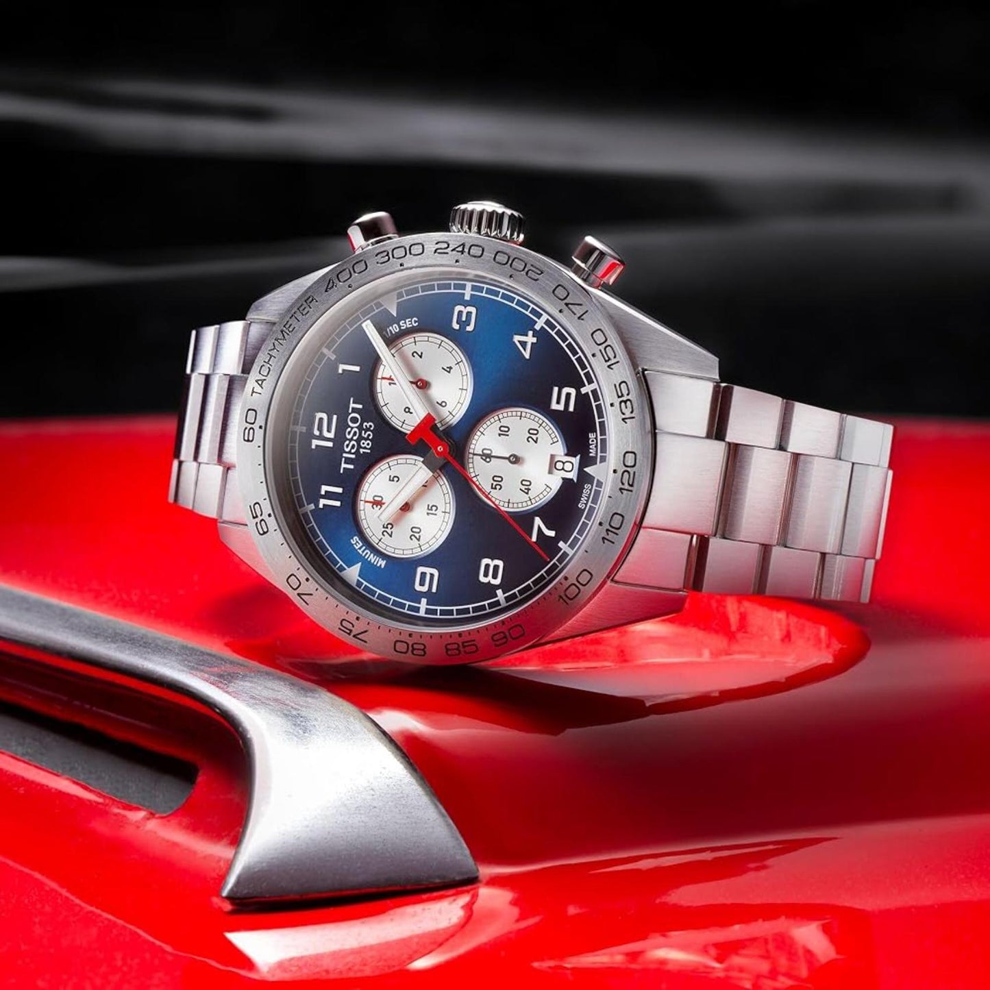 Tissot PRS 516 Chronograph T131.617.11.042.00 Swiss sport watch with blue dial, tachymeter bezel, chronograph subdials and stainless steel bracelet displayed in motorsport-inspired setting.