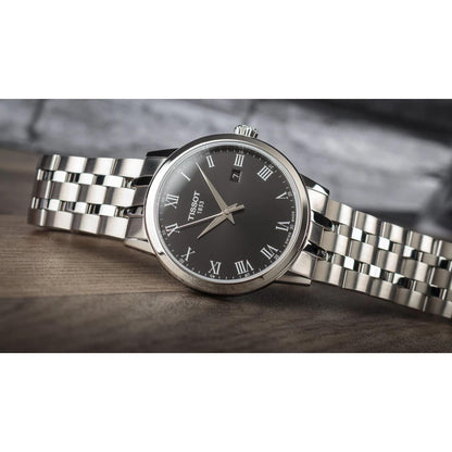 Tissot T129.410.11.053.00 quartz watch with black dial, Roman numerals and stainless steel bracelet shown in lifestyle setting.
