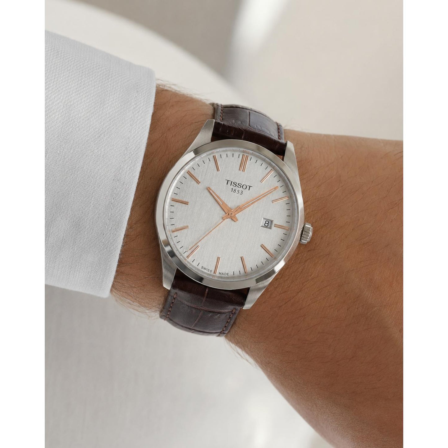Man wearing the Tissot T150.410.16.031.00 men's dress watch featuring a silver dial with rose gold-tone hour markers, stainless steel case, and brown leather strap in an elegant everyday setting.