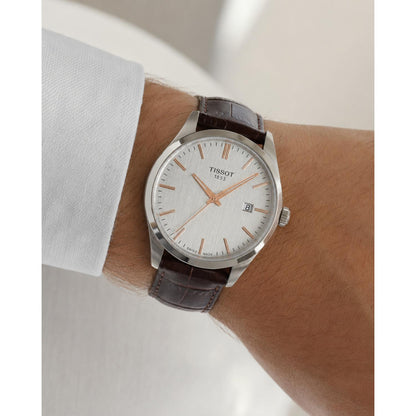 Man wearing the Tissot T150.410.16.031.00 men's dress watch featuring a silver dial with rose gold-tone hour markers, stainless steel case, and brown leather strap in an elegant everyday setting.