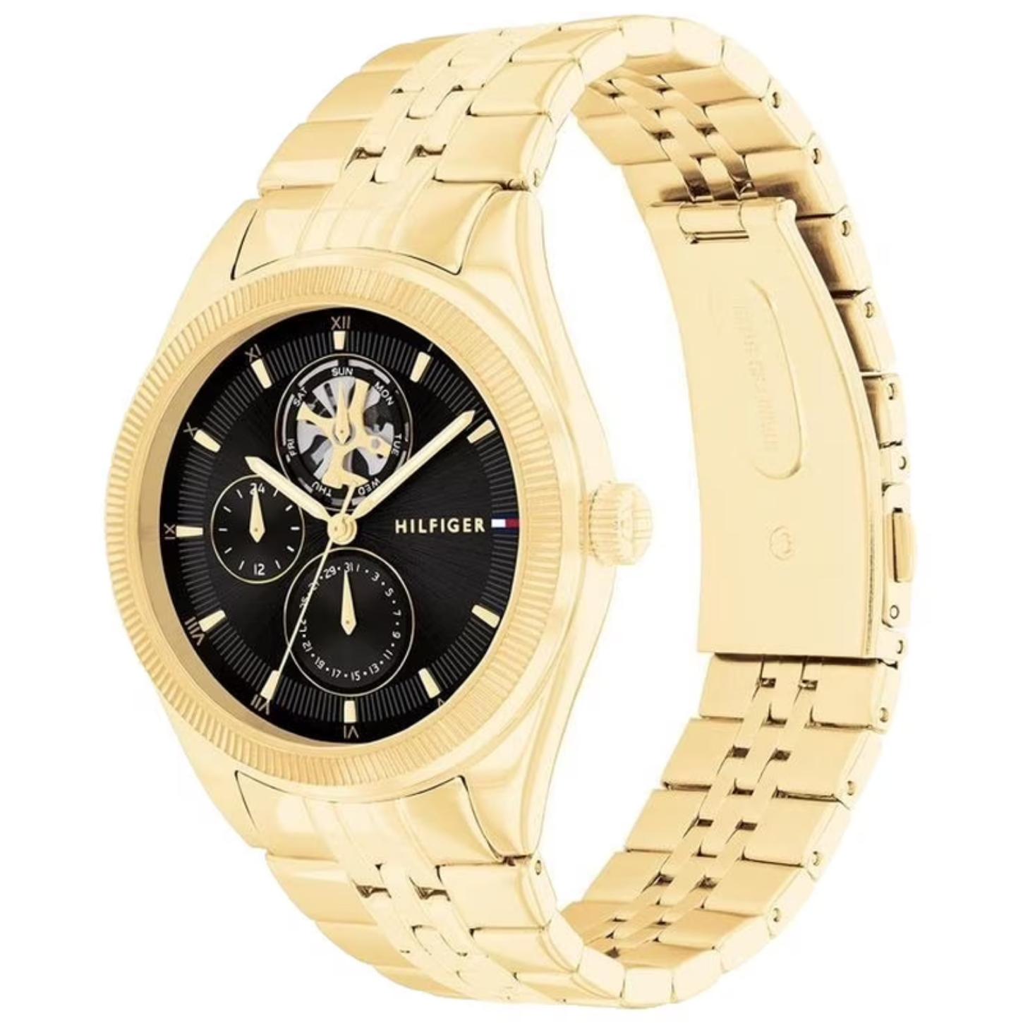 Tommy Hilfiger 1782717 women’s multifunction watch with black textured dial, open-heart display, and gold-tone stainless steel bracelet shown in an angled view.