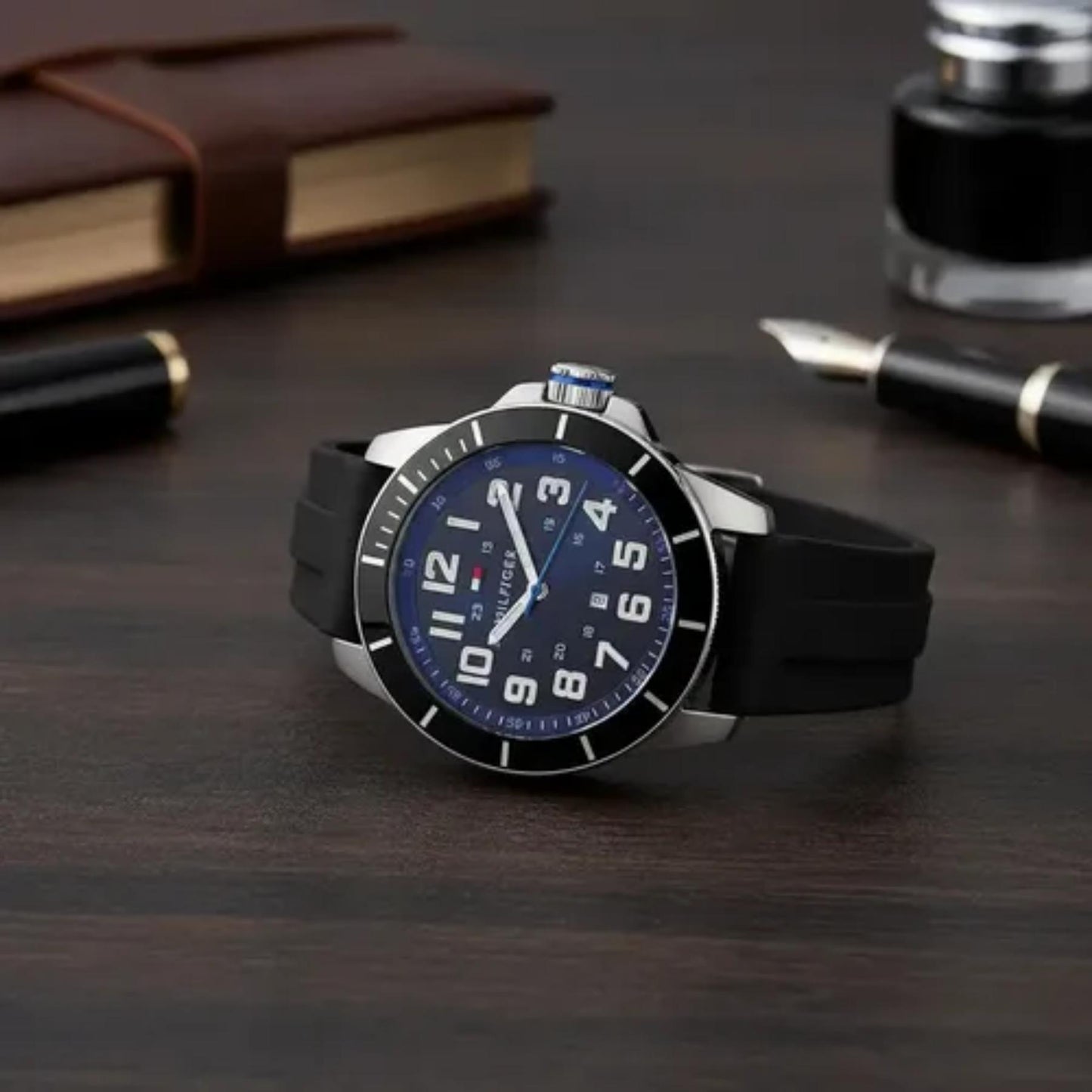 Tommy Hilfiger 179102 men’s sport watch with black dial and black silicone strap displayed on a desk beside office accessories.