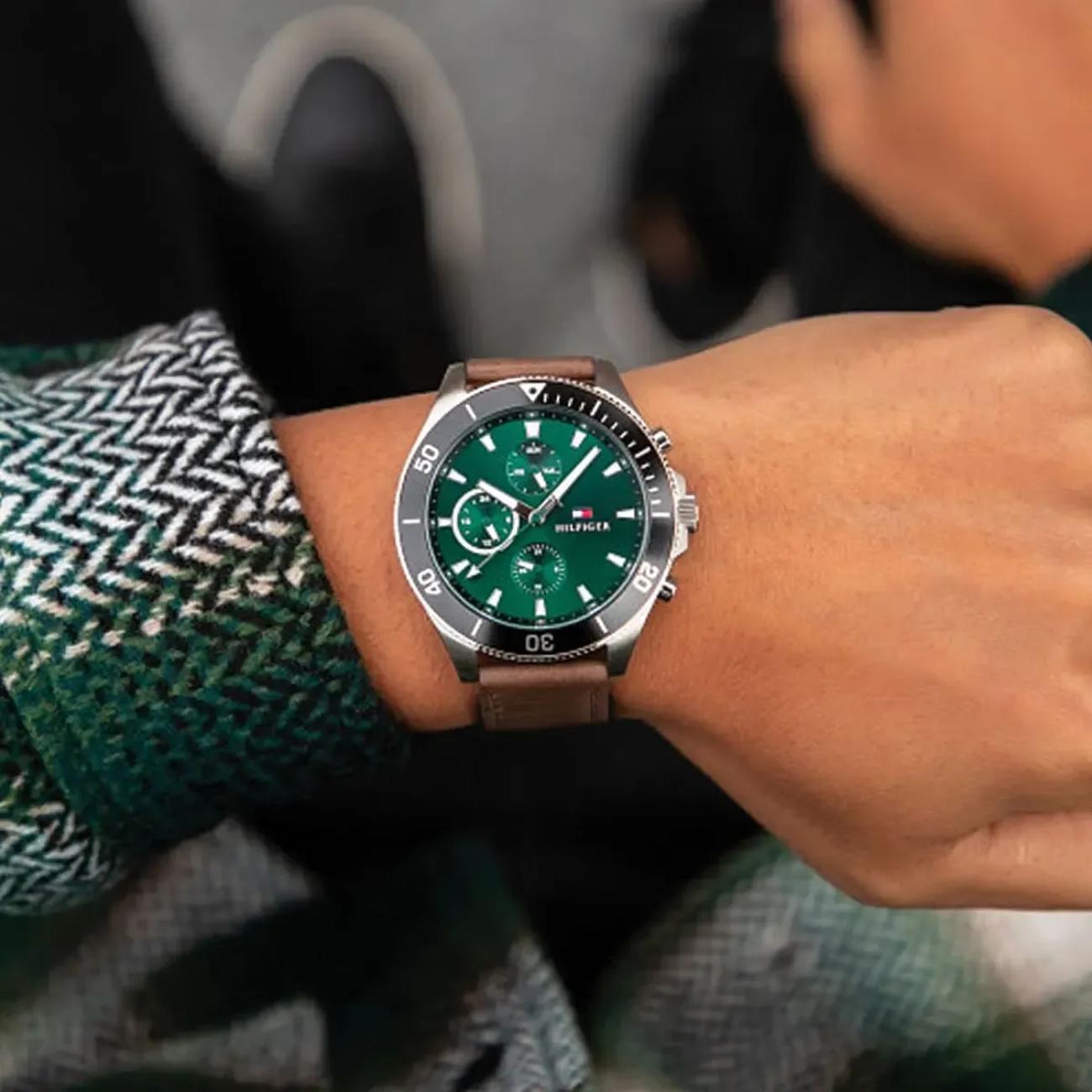 Tommy Hilfiger 1791983 men’s multifunction watch with green dial, black bezel, and brown leather strap worn on the wrist.