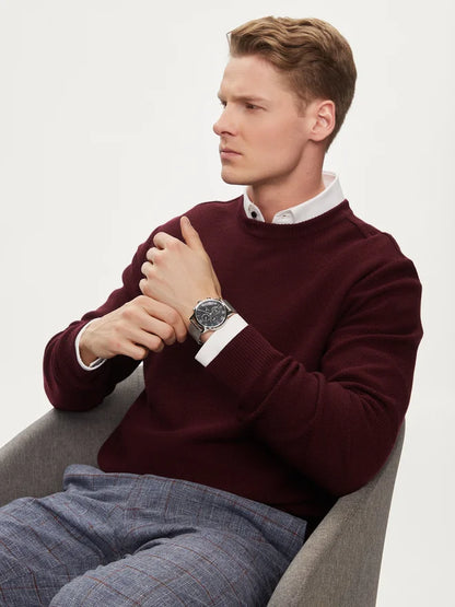 Hombre sentado con un jersey burdeos mostrando en la muñeca un reloj Tommy Hilfiger azul con correa de malla plateada.