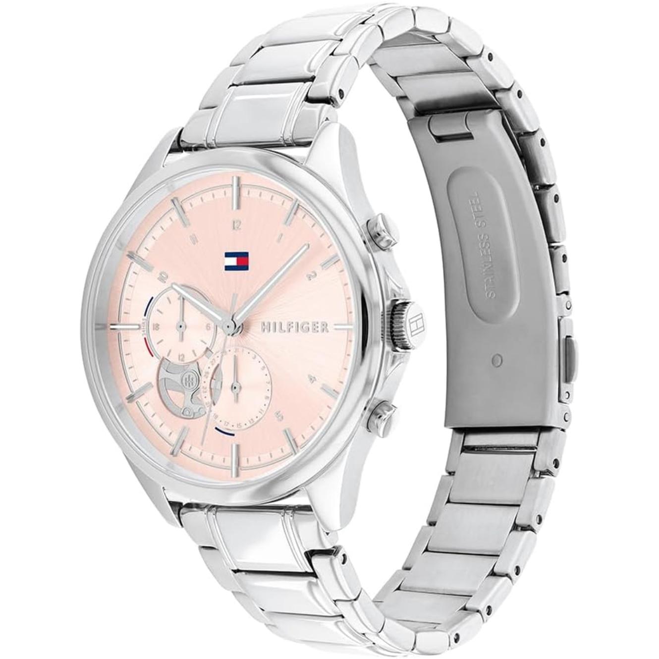 reloj Tommy Hilfiger con caja redonda plateada, esfera rosa con subesferas, pulsadores laterales y brazalete metálico visto en ángulo
