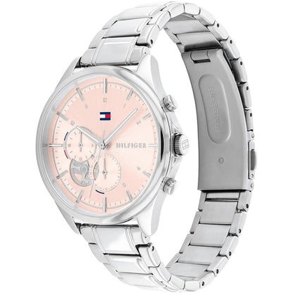 reloj Tommy Hilfiger con caja redonda plateada, esfera rosa con subesferas, pulsadores laterales y brazalete metálico visto en ángulo