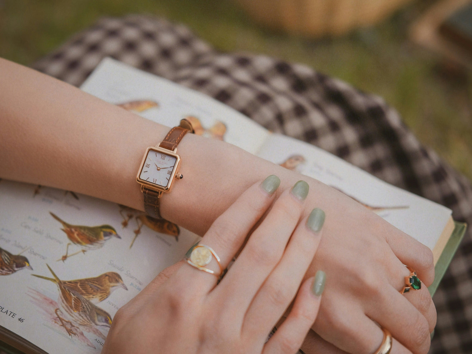 Womens rectangular watch with white dial, gold tone case and brown leather strap worn on wrist with elegant and classic design